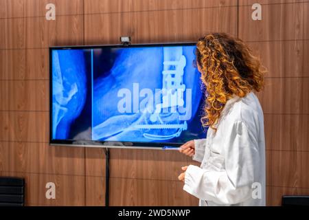 Vista posteriore di un medico donna che esamina l'anca di un paziente utilizzando la scansione a raggi X in ospedale Foto Stock