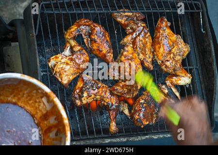 Zampa e coscia di pollo ricoperte di salsa barbecue e spezie, lo chef applica la salsa fatta in casa spazzolandola sulla carne Foto Stock