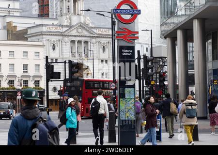 Segnaletica per le stazioni della metropolitana e ferroviaria di Victoria al livello della strada, con il Victoria Palace Theatre sullo sfondo e un autobus rosso di Londra Foto Stock