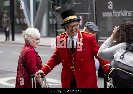 Un concierge vestito in elegante uniforme rossa tradizionale all'esterno del Rubens Hotel a Victoria, nel centro di Londra. Sta aiutando un passeggero a salire su un taxi nero Foto Stock