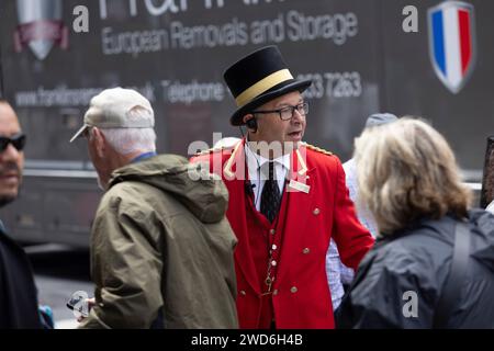 Un concierge vestito in elegante uniforme rossa tradizionale all'esterno del Rubens Hotel a Victoria, nel centro di Londra. Sta aiutando un passeggero a salire su un taxi nero Foto Stock