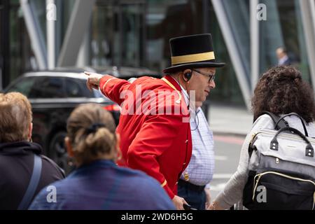 Un concierge vestito in elegante uniforme rossa tradizionale all'esterno del Rubens Hotel a Victoria, nel centro di Londra. Sta aiutando un passeggero a salire su un taxi nero Foto Stock