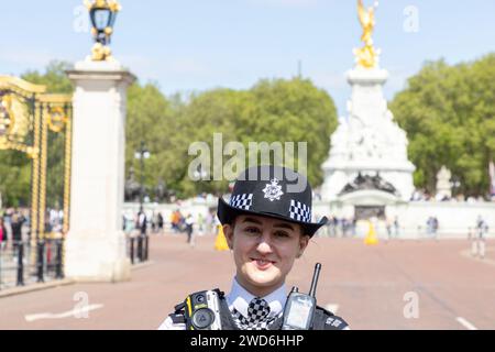 Una donna sorridente agente di polizia fuori Buckingham Palace, Londra. Dietro di lei si trova il Victoria Memorial. Foto Stock