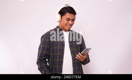 Giovane asiatico che ascolta musica su smartphone utilizzando le cuffie wireless su sfondo bianco Foto Stock