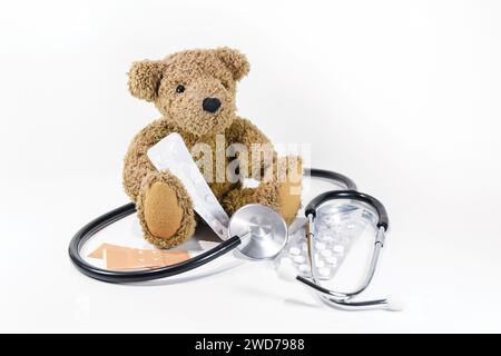 Orsacchiotto seduto con pillole, gesso e stetoscopio su sfondo bianco, assistenza sanitaria per bambini e pediatria, ma anche pericolo quando si gioca wi Foto Stock