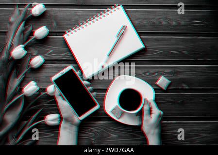 Tulipani bianchi su un tavolo di legno con un notebook vuoto, uno smartphone e una tazza di caffè in mano alle donne. Effetto glitch realtà virtuale 3D. Foto Stock
