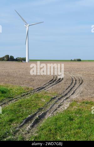 Turbina eolica in un campo appena raccolto con cingoli del trattore sotto un cielo blu. Concetto di energia pulita. Foto Stock
