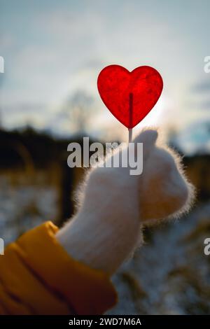 La mano di una donna in un soffice guanto bianco che regge un lecca-lecca a forma di cuore Foto Stock