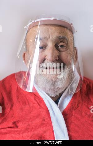 Uomo anziano che indossa una visiera protettiva e un vestito da Babbo Natale Foto Stock