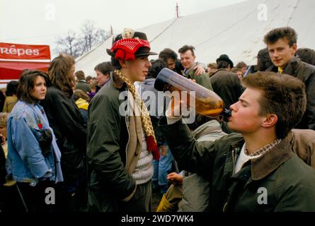 Teen Boys 1980s UK. Badminton Horse Trials. Ragazzo che beve sidro dalla bottiglia, mascotte di orso fissata al suo cappello marrone fedora. Badminton, Gloucestershire Inghilterra circa 1985 HOMER SYKES Foto Stock