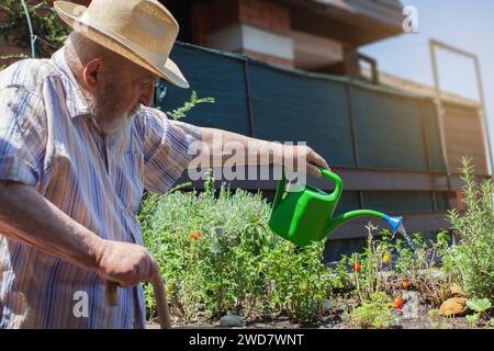 uomo anziano con canna che annaffiava fiori sulla terrazza Foto Stock