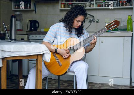 Vista frontale della giovane donna latina venezuelana, con i capelli ricci, studentessa di musica classica da sola a casa seduta concentrata sulla pratica su larga scala su acou Foto Stock