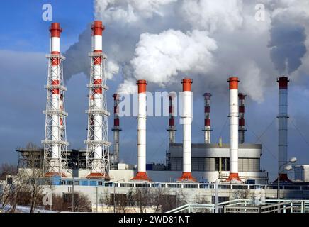 Edificio della centrale termoelettrica con molti alti tubi industriali rossi e bianchi con un denso fumo sotto il cielo invernale, con vista frontale soleggiata Foto Stock