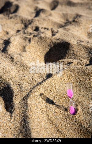 Le sabbie rosa scendono graziosamente in una clessidra sul mare, catturando momenti fugaci di tranquilla bellezza sulla spiaggia Foto Stock