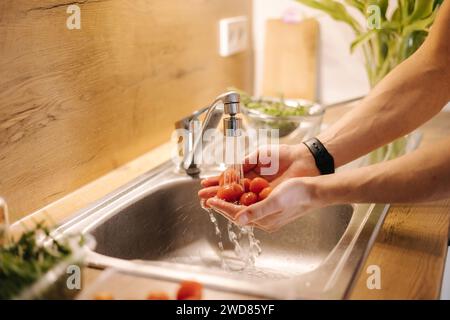 Primo piano della mano umana prendere pomodori ciliegini rossi in cucina Foto Stock