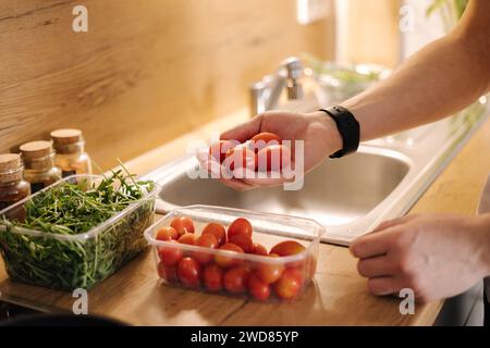 Primo piano della mano umana prendere pomodori ciliegini rossi in cucina Foto Stock