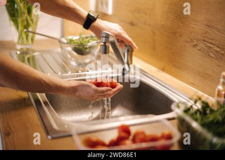 Primo piano della mano umana prendere pomodori ciliegini rossi in cucina Foto Stock