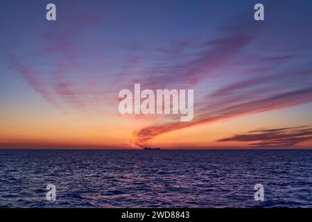 Splendida alba nel mare con un cielo colorato rosa, giallo, arancione e viola, oceano blu e sagoma di una nave all'orizzonte. Foto Stock