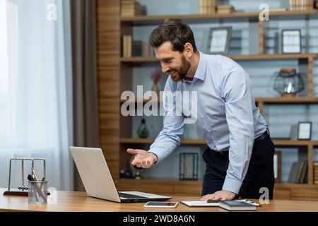 Un professionista maschio maturo sorridente impegnato in attività aziendali da un ufficio domestico ben organizzato con un computer portatile. Foto Stock