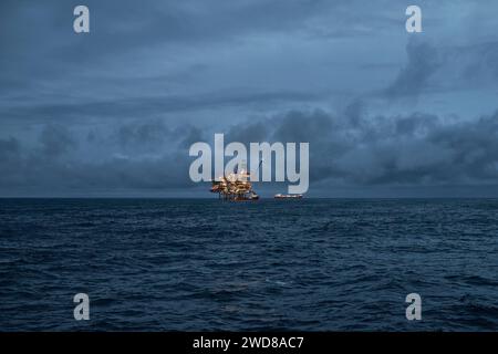 Vista panoramica del giacimento di petrolio offshore in mare, la mattina presto, con piattaforma di perforazione di petrolio e gas e petroliera all'orizzonte. Foto Stock