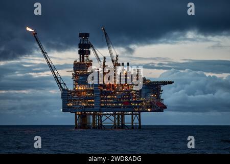 Vista ravvicinata della piattaforma di perforazione illuminata di notte, con cielo blu scuro nell'oceano blu profondo. Foto Stock