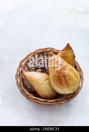 Deliziosa Samsa con agnello e spezie cotte al tandoor. Samsa in un piccolo cesto su fondo di pietra Foto Stock