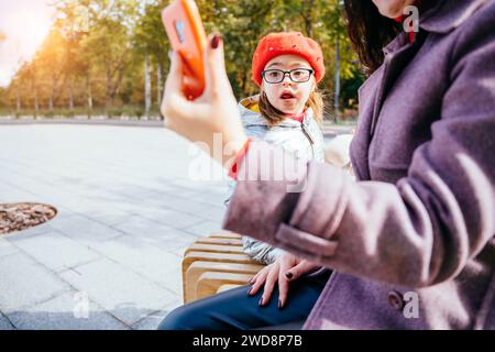 Bruna giovane madre che mostra cartoni animati a disabili bambina adorabile sullo smartphone. Foto Stock