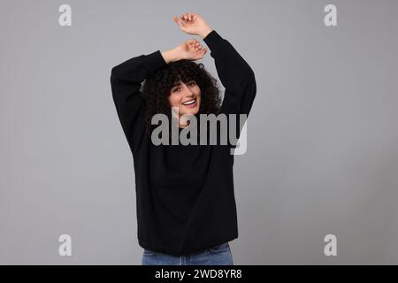 Giovane donna felice con un elegante maglione nero su sfondo grigio chiaro Foto Stock