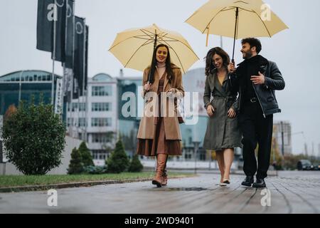 Un allegro trio ama fare una passeggiata di una giornata piovosa in città, condividendo sorrisi e tenendo ombrelli gialli sullo sfondo urbano. Foto Stock