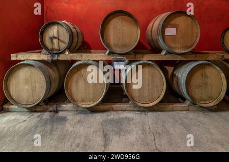 Alcune barriques di legno per l'invecchiamento del vino sono disposte su due livelli in una cantina toscana Foto Stock