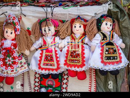 Bambole vestite con costumi tradizionali rumeni, adagiate su materiali ricamati ed esposte per la vendita. Foto Stock