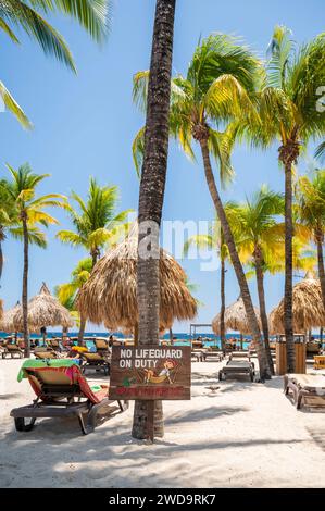 Tipica spiaggia caraibica, con un divertente cartello "No Lifeguard" inchiodato ad una palma Foto Stock