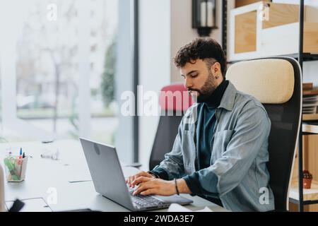 Un uomo nella moderna zona degli uffici, che si affida al suo portatile, affronta le attività con concentrazione e dinamismo tecnologico. Il lavoro è reale Foto Stock