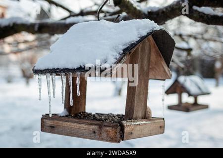 Alimentatore per uccelli in legno con ghiaccio ghiacciato e innevato appeso su un albero in inverno Foto Stock