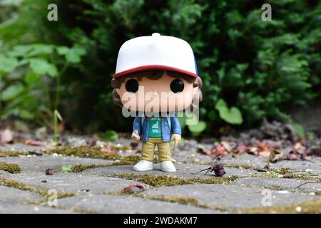 Funko Pop action figure di Dustin Henderson con bussola della famosa serie TV Netflix Stranger Things. Foglie verdi, strada in pietra mossy, giardino primaverile Foto Stock