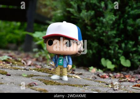 Funko Pop action figure di Dustin Henderson con bussola della famosa serie TV Netflix Stranger Things. Foglie verdi, strada in pietra mossy, giardino primaverile Foto Stock