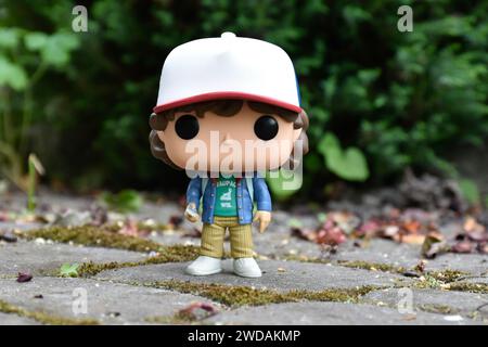 Funko Pop action figure di Dustin Henderson con bussola della famosa serie TV Netflix Stranger Things. Foglie verdi, strada in pietra mossy, giardino primaverile Foto Stock