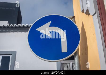 Svolta a sinistra, cerchio blu con freccia bianca sul lato di un edificio Foto Stock