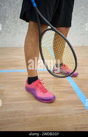 Uomo con pantaloni felpa e sneakers neri che reggono una racchetta da squash Foto Stock