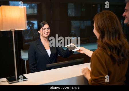 Una receptionist sorridente che prende il passaporto da una donna vicino all'uomo alla reception dell'hotel Foto Stock
