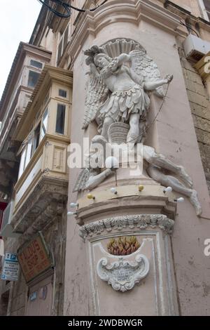 San Michele Arcangelo uccide il diavolo che si trova ai suoi piedi. Statua fregio su edifici con balconi coperti a la Valletta, Malta, HOMER SYKES anni '2024 2020 Foto Stock