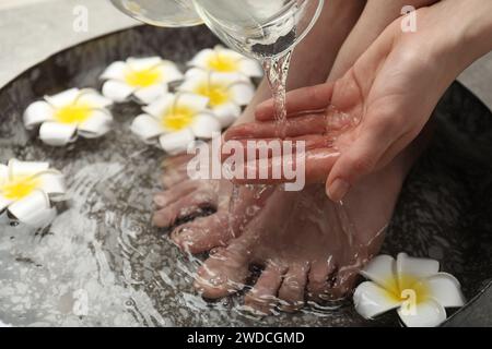 Donna che versa acqua sulla mano mentre ammorbidisce i piedi nella ciotola, primo piano. Trattamento spa Foto Stock