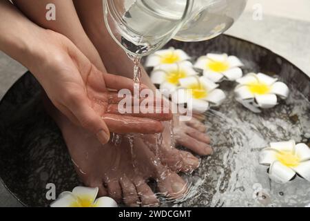 Donna che versa acqua sulla mano mentre ammorbidisce i piedi nella ciotola, primo piano. Trattamento spa Foto Stock