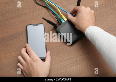 Uomo con smartphone che si connette a Internet tramite router Wi-Fi al tavolo di legno, primo piano Foto Stock