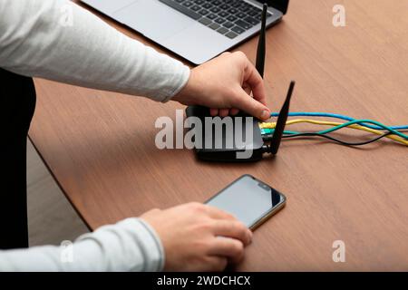 Uomo con smartphone che si connette a Internet tramite router Wi-Fi al tavolo di legno, primo piano Foto Stock