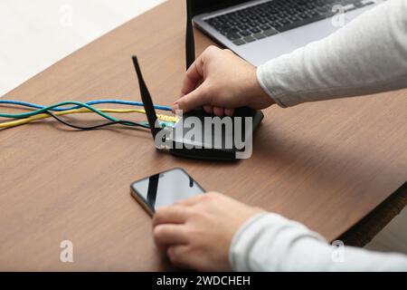 Uomo con smartphone che si connette a Internet tramite router Wi-Fi al tavolo di legno, primo piano Foto Stock