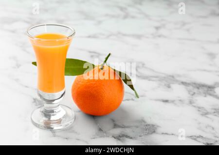 Delizioso liquore al mandarino in bicchierino e frutta fresca su un tavolo in marmo bianco, primo piano. Spazio per il testo Foto Stock