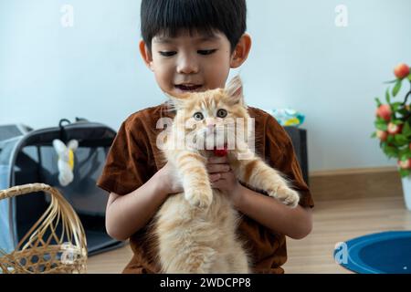 Un piccolo ragazzo asiatico tiene amorevolmente un gattino arancione. Foto Stock