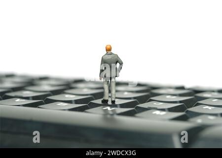 Fotografia di figure giocattolo in miniatura. Illustrazione del concetto di business. Un uomo d'affari pensivo che si trova sopra la tastiera di un notebook. Isolato su b bianco Foto Stock