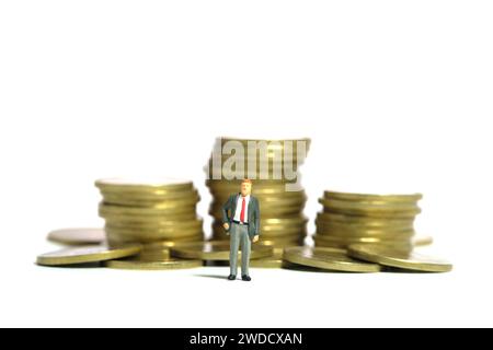 Fotografia di figure giocattolo in miniatura. Concetto di consulenza sugli investimenti. Un uomo d'affari in piedi davanti al mucchio di monete. Isolato su uno sfondo bianco Foto Stock